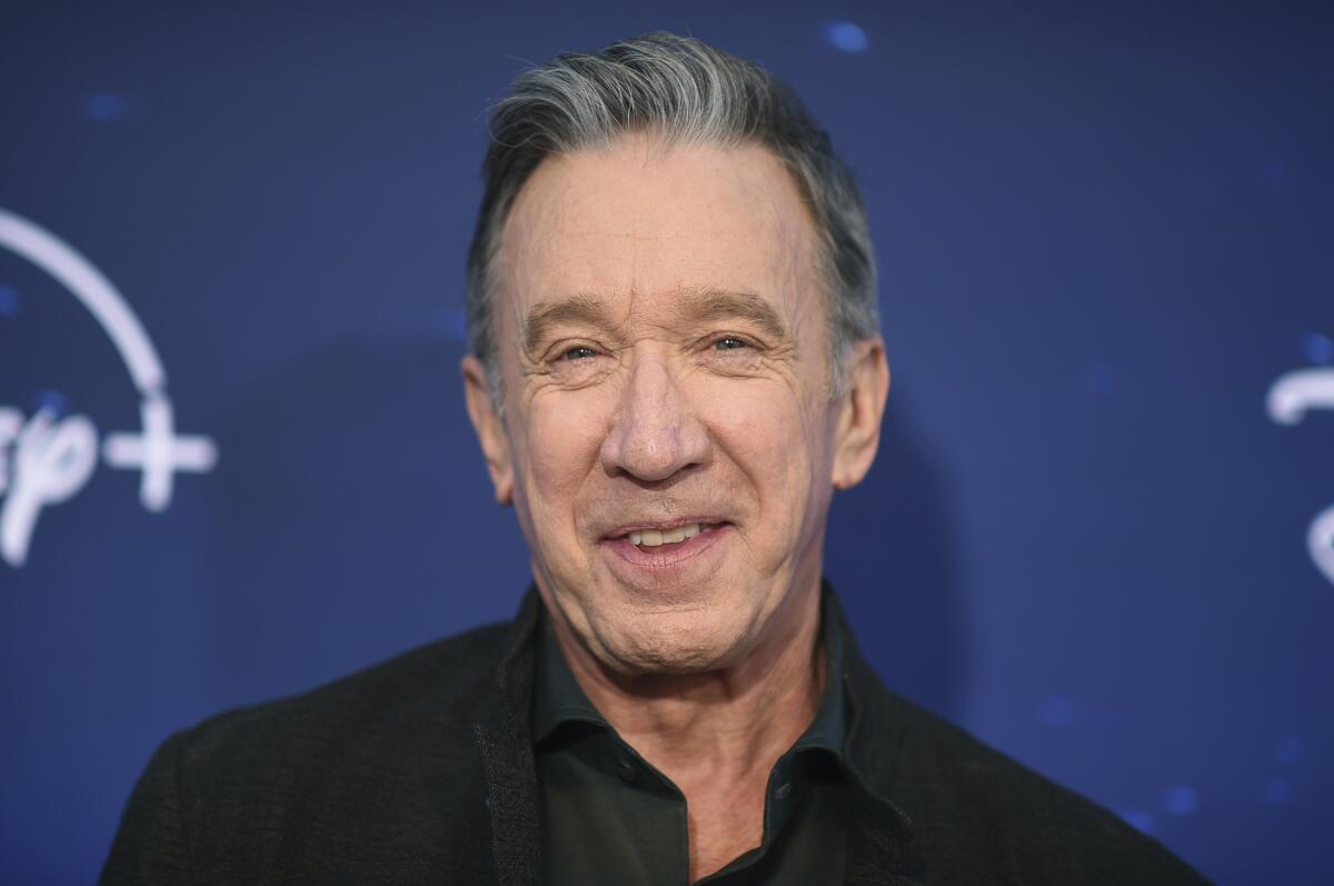 Tim Allen, with short gray hair and a black collared shirt, arrives at an event.