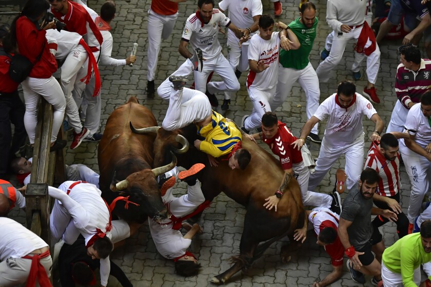 FILE - Runners fall as another is tossed by a fighting bull during the running of the bulls at the San Fermin festival in Pamplona, northern Spain, Monday, July 11, 2022. Pamplona is once again a sea of red and white as the frenzied madness of the San Fermín running of the bulls festival returns with adrenaline, emotion and passion following a two-year suspension due to the coronavirus pandemic. (AP Photo/Alvaro Barrientos, File)