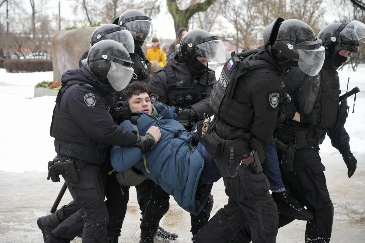 Police in riot gear carry a man who tried to lay flowers at a monument in St. Petersburg, Russia.