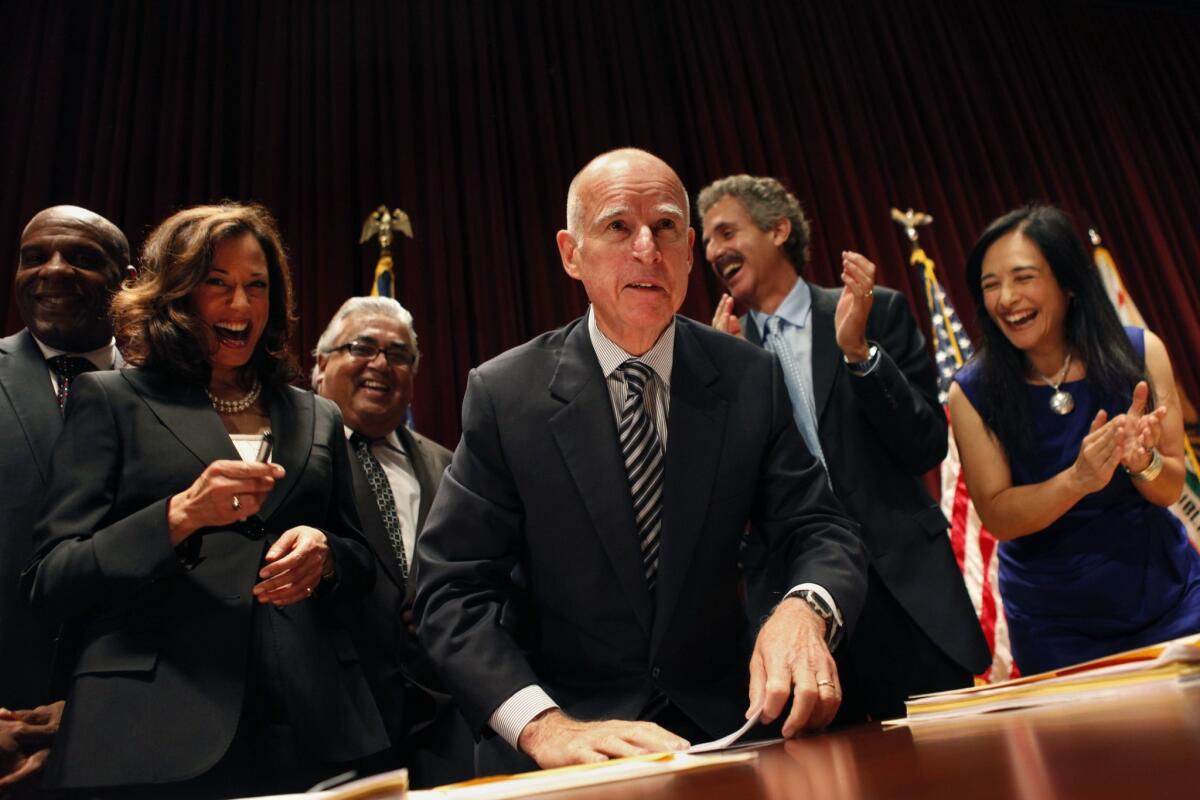 Gov. Jerry Brown, center, flanked by Atty. Gen. Kamala Harris, left, and Maria Cabildo of the East Los Angeles Community Corp., right, signs the Homeowner Bill of Rights foreclosure legislation at the Ronald Reagan State Building in July 2012 in Los Angeles.