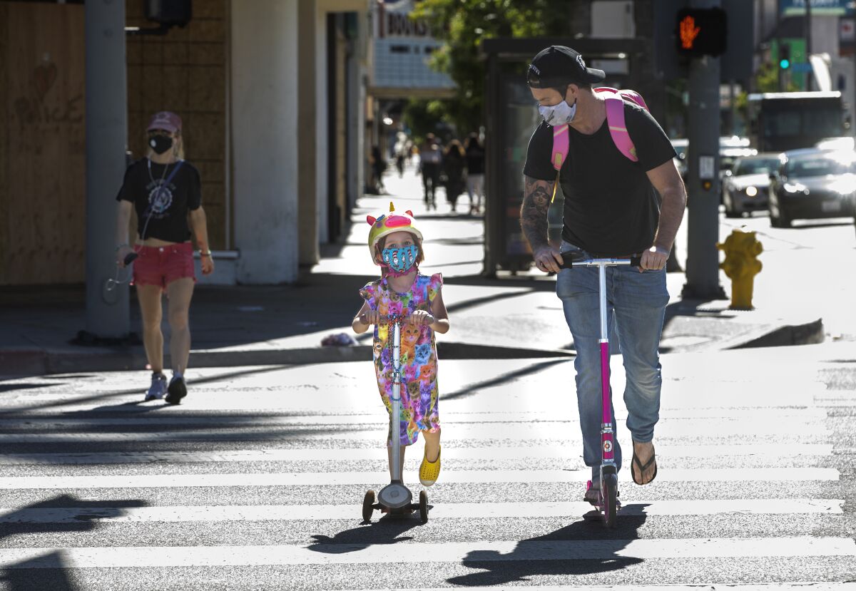 People wear protective masks while riding scooters in Studio City
