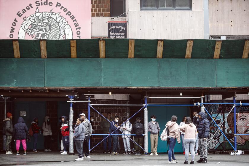Un grupo de estudiantes espera en las instalaciones académicas para recibir laptops para tomar clases a distancia en la escuela secundaria Lower East Side, el jueves 19 de marzo de 2020, en Nueva York. (AP Foto/John Minchillo)