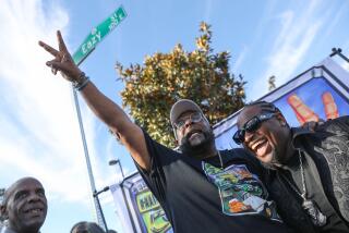 Compton , CA - November 22: Alonzo Williams, left, puts up the peace symbol as he celebrates alongside Eric Wright Jr. during a ceremony honoring Eazy-E with his own street named Eazy Street; at Auto Drive South on Wednesday, Nov. 22, 2023 in Compton, CA. (Michael Blackshire / Los Angeles Times)