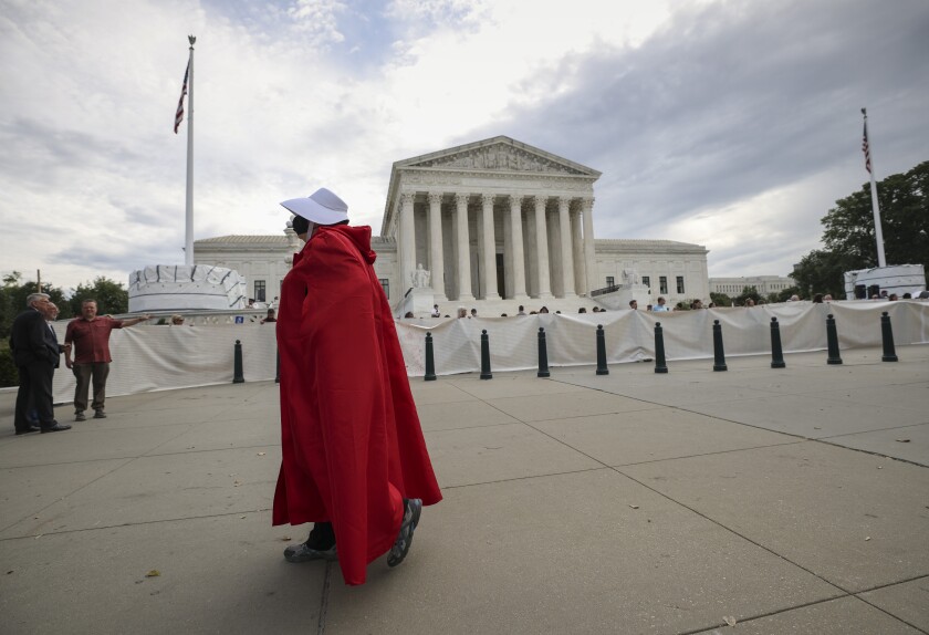 A woman dressed in a "Handmaid's Tale" costume with the Supreme Court in the background. 