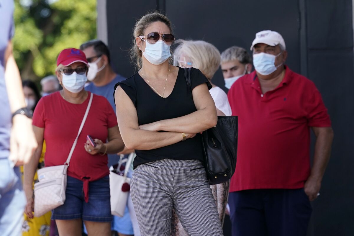 People stand in line for early voting at the John F. Kennedy Library, Tuesday, Oct. 27, 2020, in Hialeah, Fla. Masks are required at some polling places around the country and strongly encouraged in most others as a basic precaution to help keep poll works and others safe from the fast-spreading coronavirus. But mandates tying a face covering to casting a ballot are sure to lead to confrontations on Election Day, and those will almost certainly grab wide attention if they arise in any of the presidential battleground states. (AP Photo/Lynne Sladky)