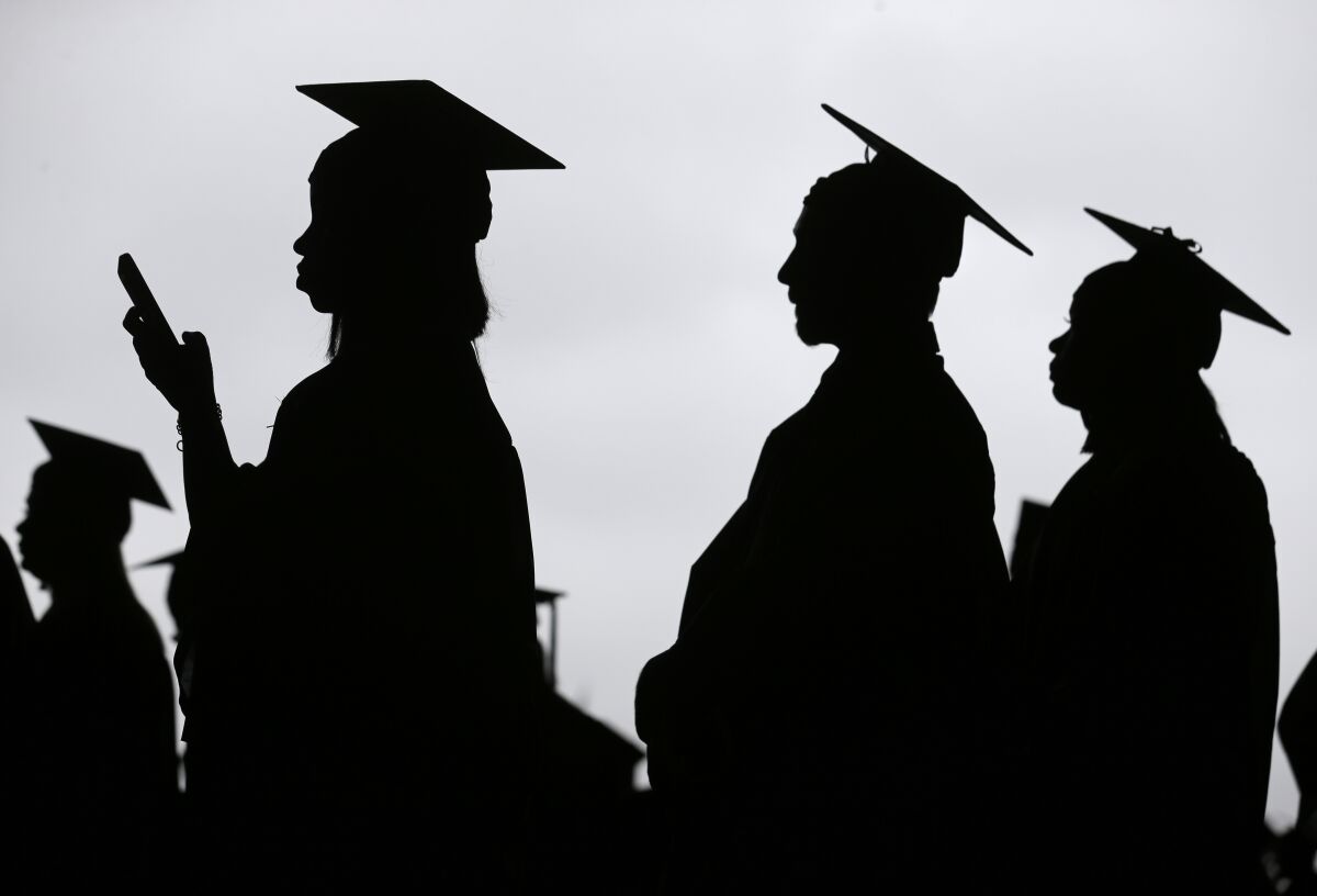 Graduates seen in silhouette line up at a college commencement ceremony