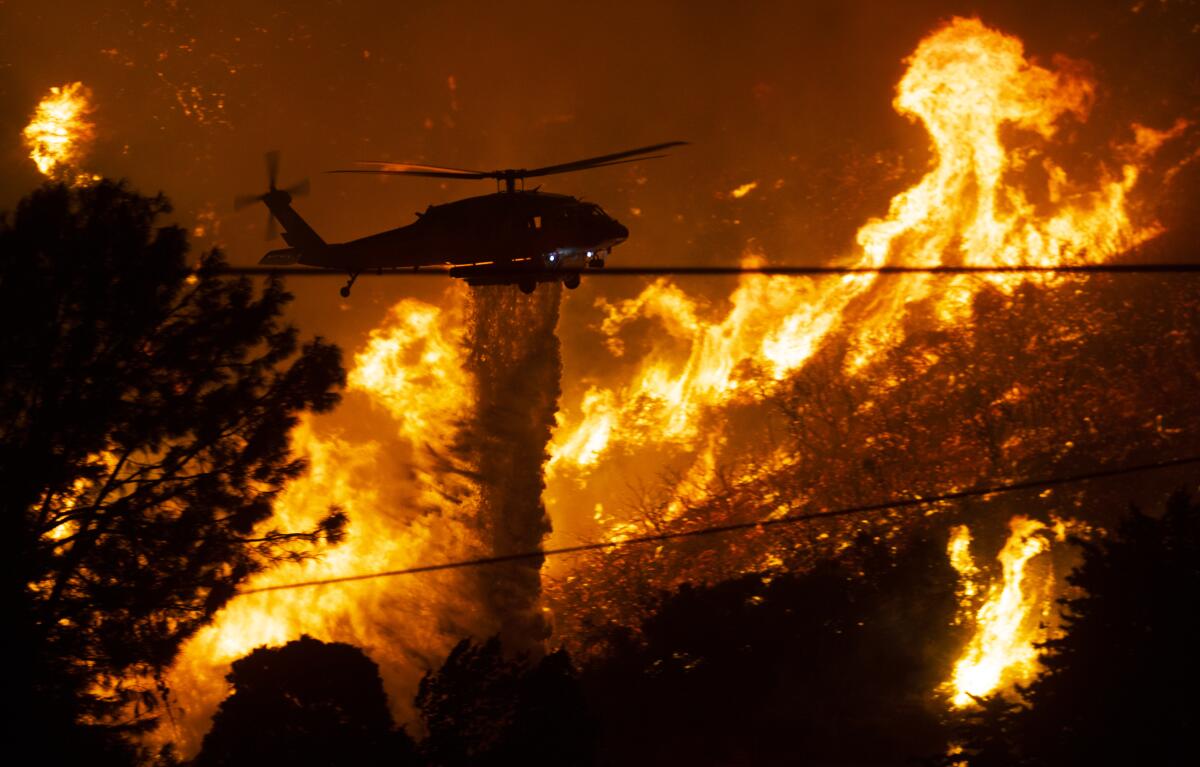 A firefighting helicopter drops water as flames from the Lake fire rage in the Angeles National Forest