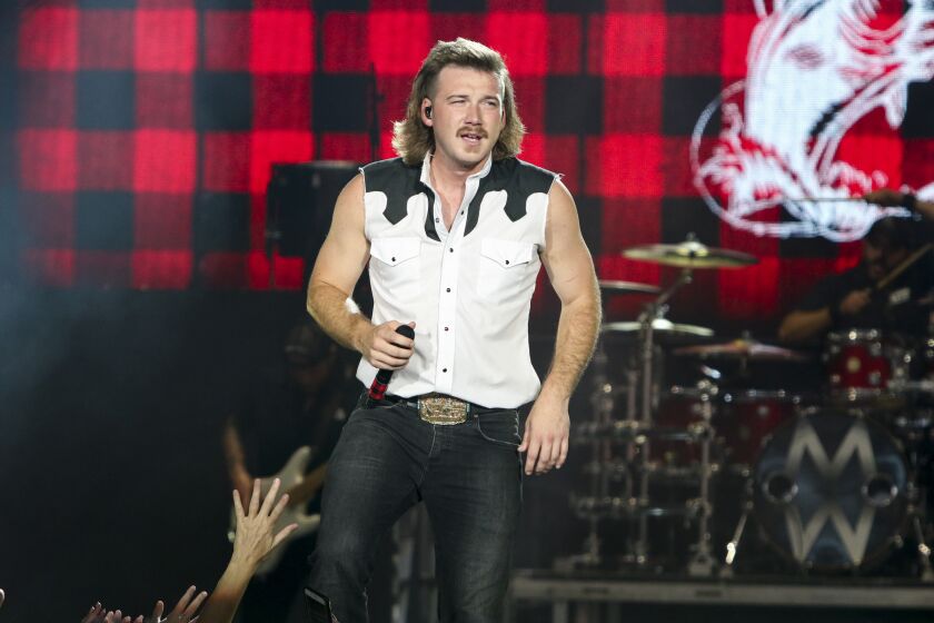 A man with a mullet hair style wearing a vest performs onstage