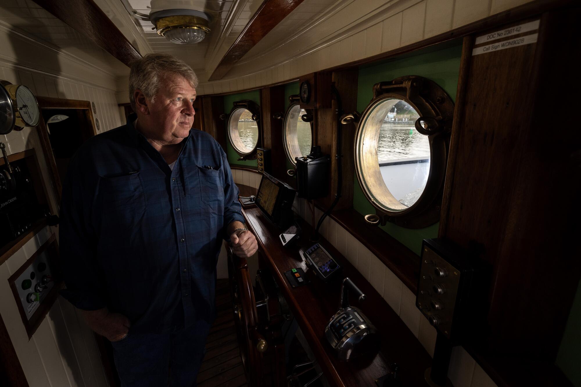 A man looks out from a porthole on a wooden vessel.