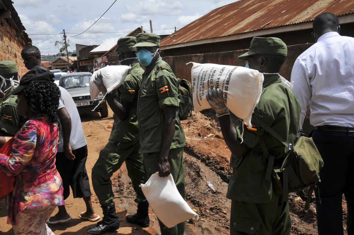 Miembros de las fuerzas armadas de Uganda distribuyen comida a gente afectada por la cuarentena para combatir el coronavirus en el suburbio Bwaise de la capital, Kampala, Uganda, el sábado 4 de abril de 2020. (AP Foto/Ronald Kabuubi)