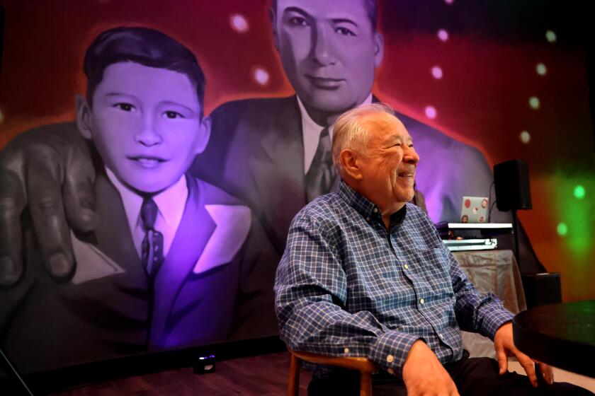 NORWALK, CA - SEPTEMBER 4, 2024 - A smiling Moctesuma Esparza, 75, sits in front of a mural, by Robert Vargas, of he and his father Francisco Esparza at the Milagro Cinemas in Norwalk on September 4, 2024. Esparza, a movie producer and entertainment executive, is the owner of Milagros Theater which he created to serve what he says is an underserved Latino audience. As a child, Esparza and his father would spend Monday's, his father's only day off, going to the movies on Broadway in downtown Los Angeles. Esparza, has produced many films including, "The Milagro Beanfield War," and "Selena." (Genaro Molina/Los Angeles Times)