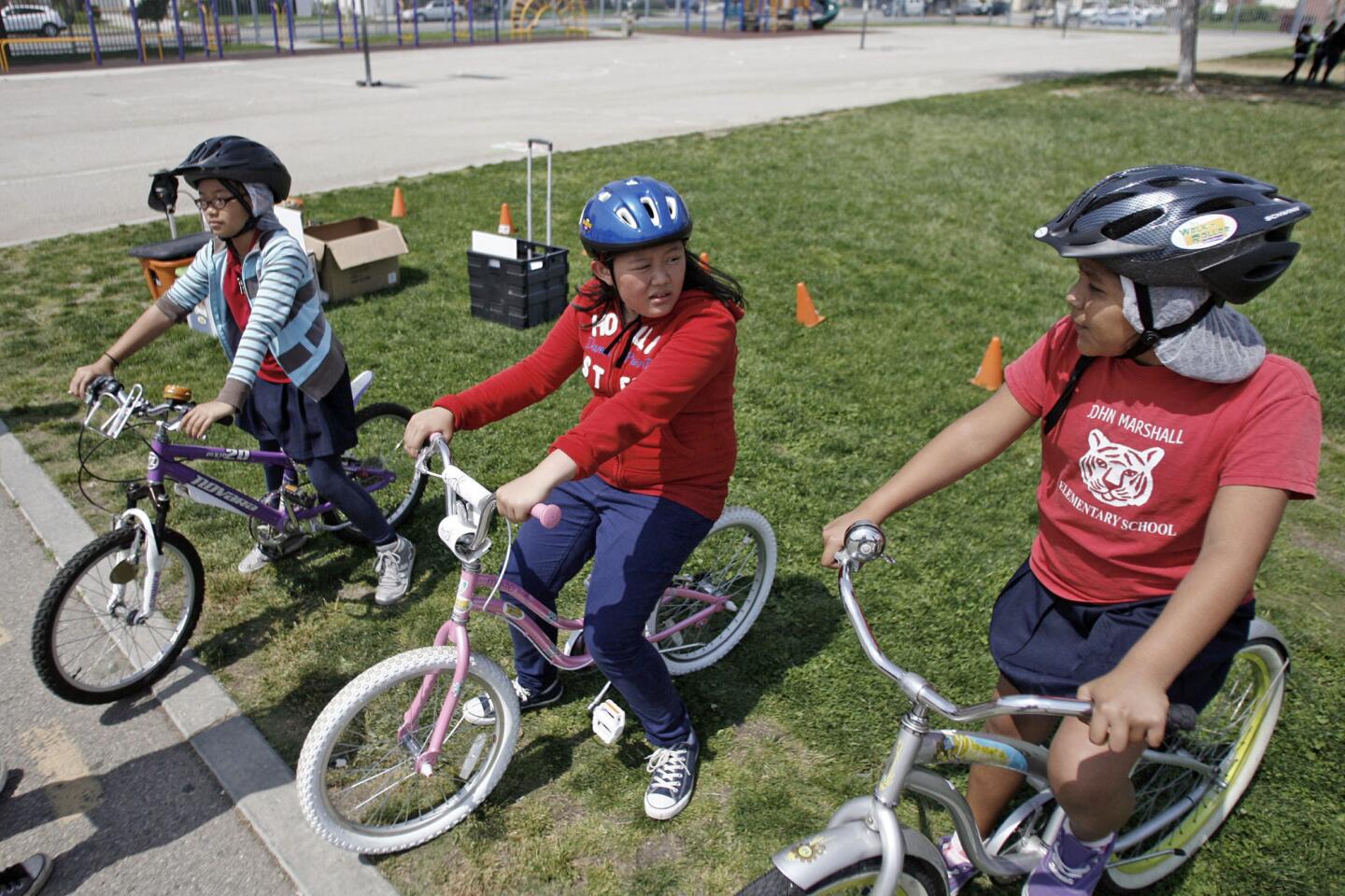 Fifth-grade students Francine Fernandez, 10, from left, Jenelle Velsa, 11, and Dulce Aguilar, 11, rest on their bikes before learning safety tips during bike skills safety week, which took place at John Marshall Elementary School in Glendale on Friday, April 5, 2013. 93 students from the school participated in the event.