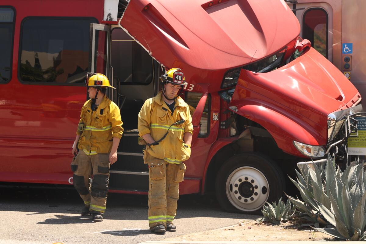 Two firefighters stand next to a damaged red bus.