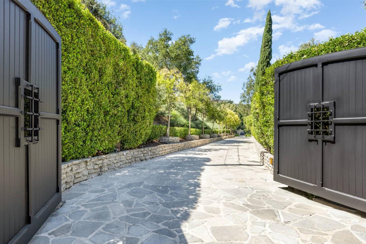 The tree-lined stone driveway accessed behind large dark gates.