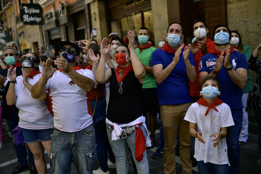 FILE In this Saturday, June 20, 2020 file photo, residents wear faces mask to protect against coronavirus and wear San Fermin's red kerchief as people march the route of the running of the bulls while a singer performs a San Fermin's festival song, in Pamplona, northern Spain. Spain reopened its borders to European tourists Sunday, June 21, 2020 in a bid to kickstart its economy while Brazil and South Africa struggled with rising coronavirus infections. At a campaign rally, President Donald Trump said he told the U.S. government to reduce testing for the virus, apparently to avoid unflattering statistics ahead of the U.S. election in November. (AP Photo/Alvaro Barrientos, File)