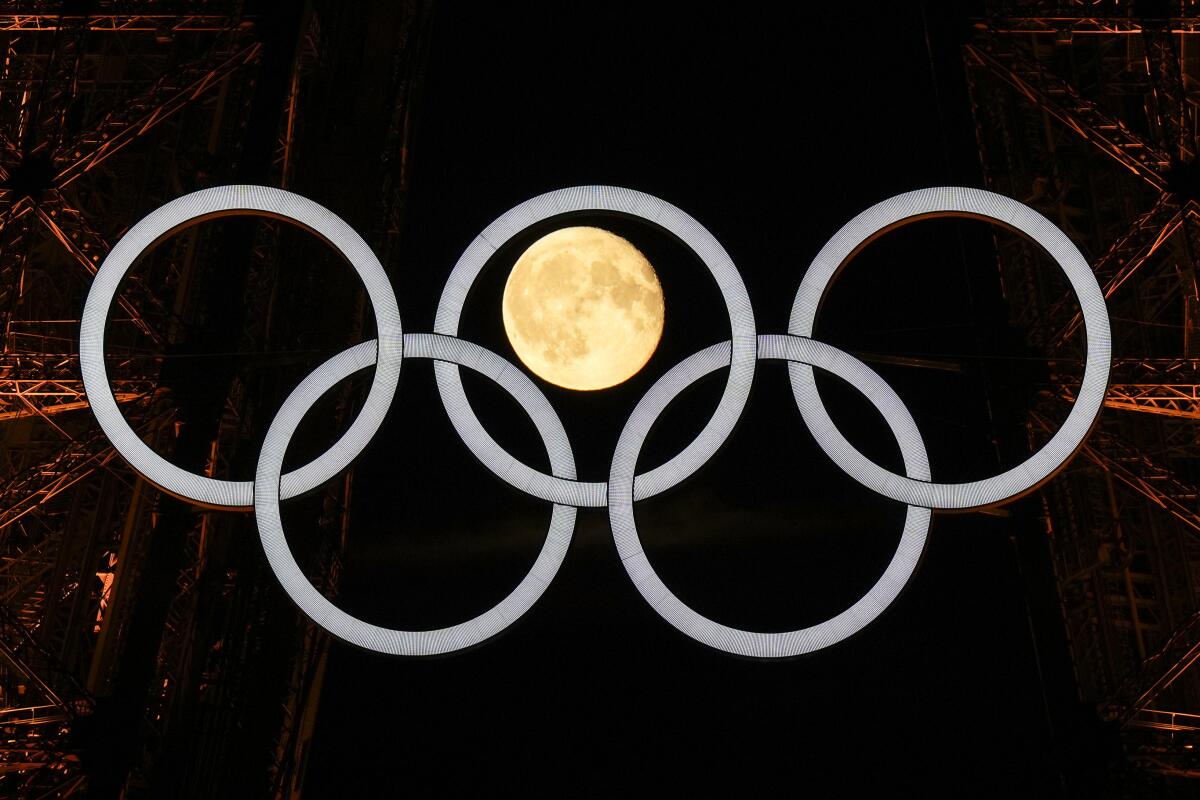 A full moon rises behind the Olympic rings hangin 