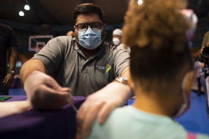 El secretario del Departamento de Salud, Carlos Mellado, aplica a una menor una dosis de la vacuna de Pfizer contra el COVID-19 en el Coliseo Tomás Dones, en Fajardo, Puerto Rico, el sábado 8 de enero de 2022. (AP Foto/Carlos Giusti)