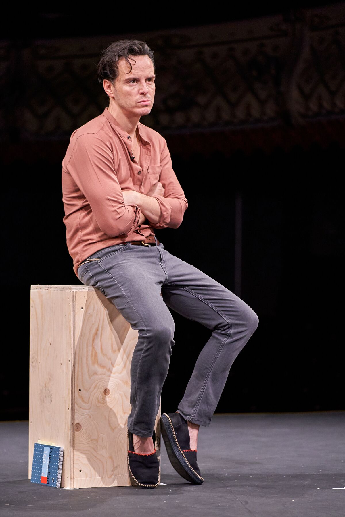 Andrew Scott sits on a wooden box in the play "Three Kings."