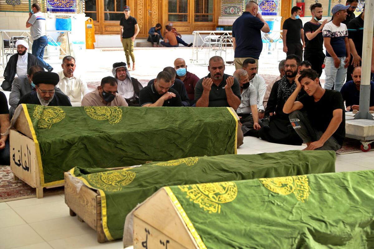 People kneel and mourn alongisde coffins.