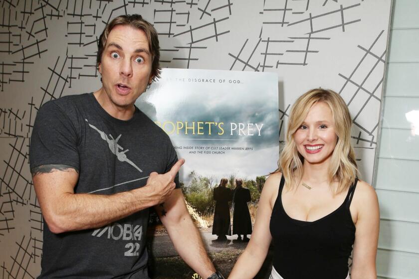 Dax Shepard and Kristen Bell posing in front of a film poster while holding hands. 