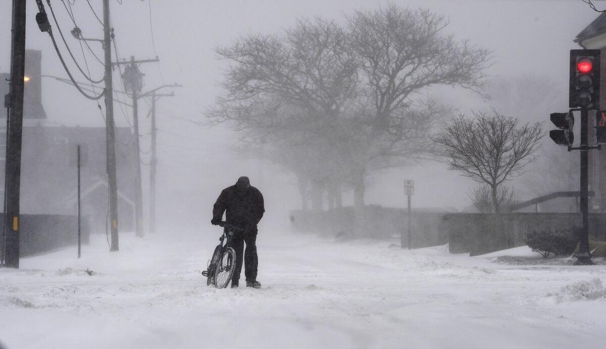 A cyclist walks his bicycle in white-out conditions in Hyannis, Mass., on Wednesday. A storm blanketed the area of Cape Cod, Mass., with up to six inches of snow and winds topping 60 mph, creating hazardous driving conditions and power outages.