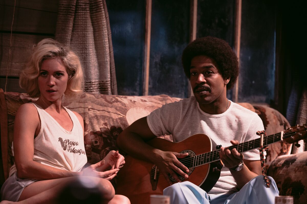 A woman sits on a couch, with a guitar-playing man next to her. 