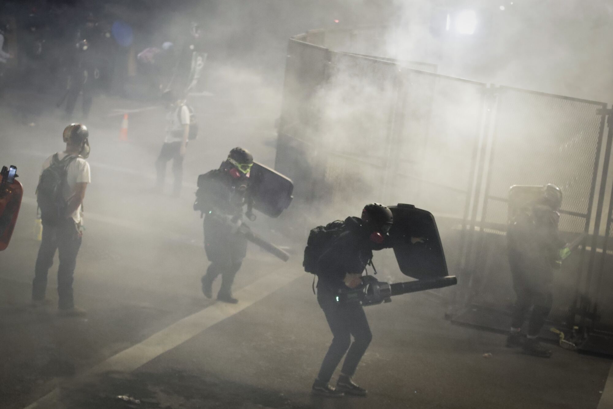 Demonstrators use leaf blowers to blow back tear gas launched by federal officers during a protest in Portland, Ore.