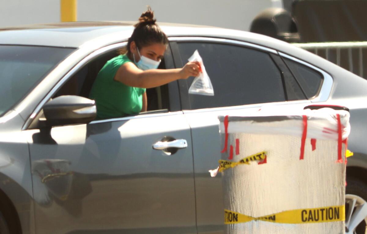 A woman deposits her coronavirus test in a bin at the COVID-19 testing site at the Forum parking lot in Inglewood.