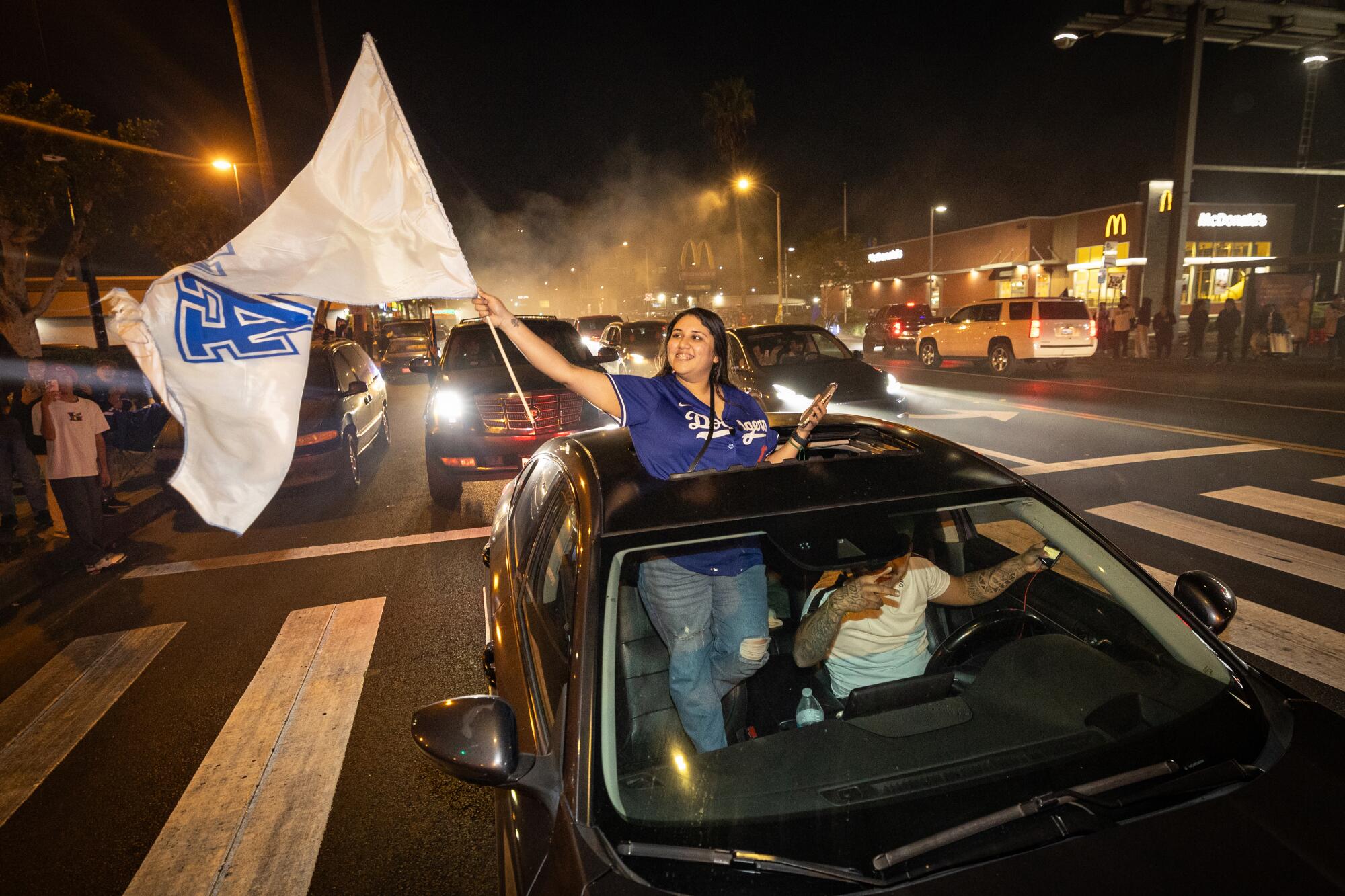 Ain't no occasion like an East L.A. Dodgers occasion — and it did not cease 2 A woman standing in a car, halfway through the sunroof, holds a large L.A. Dodgers fan