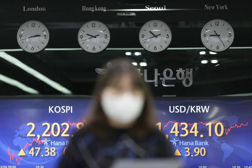 A currency trader walks by the screens showing the Korea Composite Stock Price Index (KOSPI), left, and the foreign exchange rate between U.S. dollar and South Korean won at a foreign exchange dealing room in Seoul, South Korea, Tuesday, Oct. 4, 2022. Asian shares rose Tuesday, encouraged by a rally in U.S. shares after some weak economic data raised hopes that the Federal Reserve might ease away from aggressive interest rate hikes. (AP Photo/Lee Jin-man)