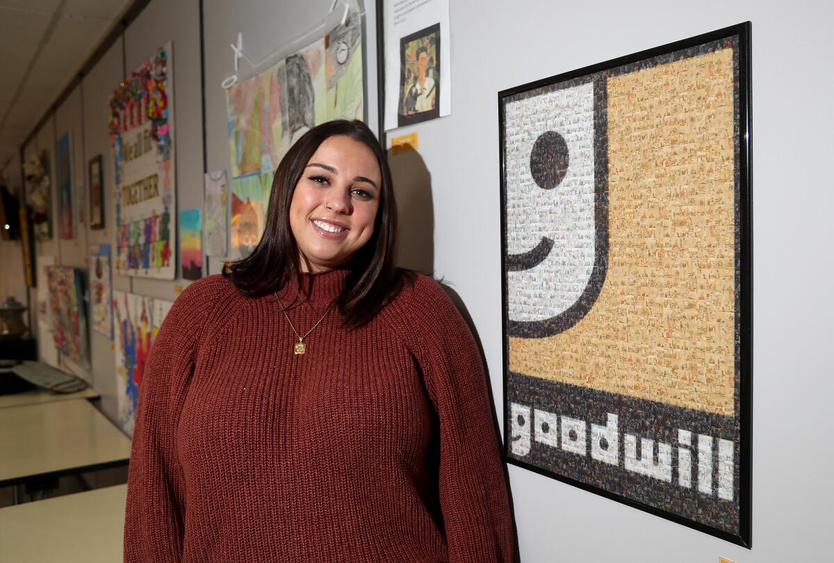 Kristiana Gringras stands next to her Goodwill logo filled with mini photos of fellow team members.