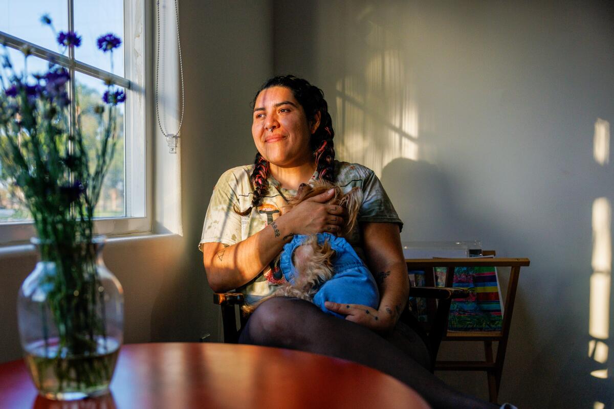 A person sitting in a chair with his dog, looking out the window.