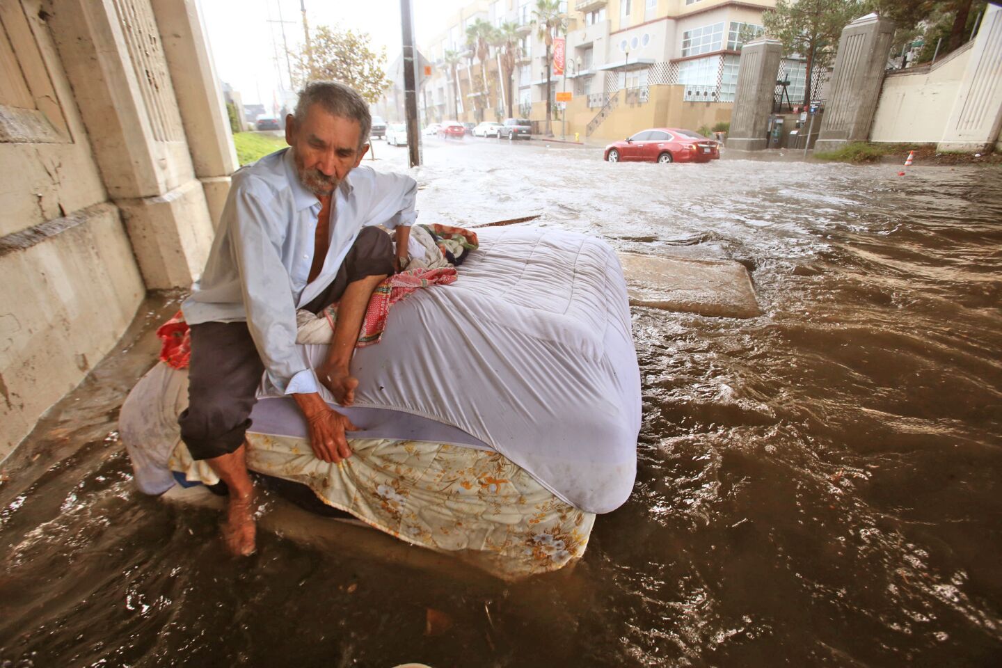 Felipe Flores Lopez, 59, tries to stay afloat on a bed at his homeless encampment as rainwater floods a section of Avenue 26.