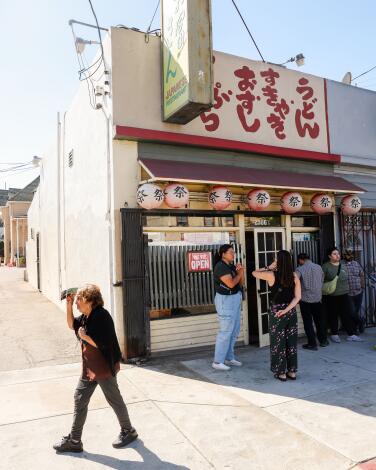 People wait outside a small storefront with Japanese lanterns and signage out front