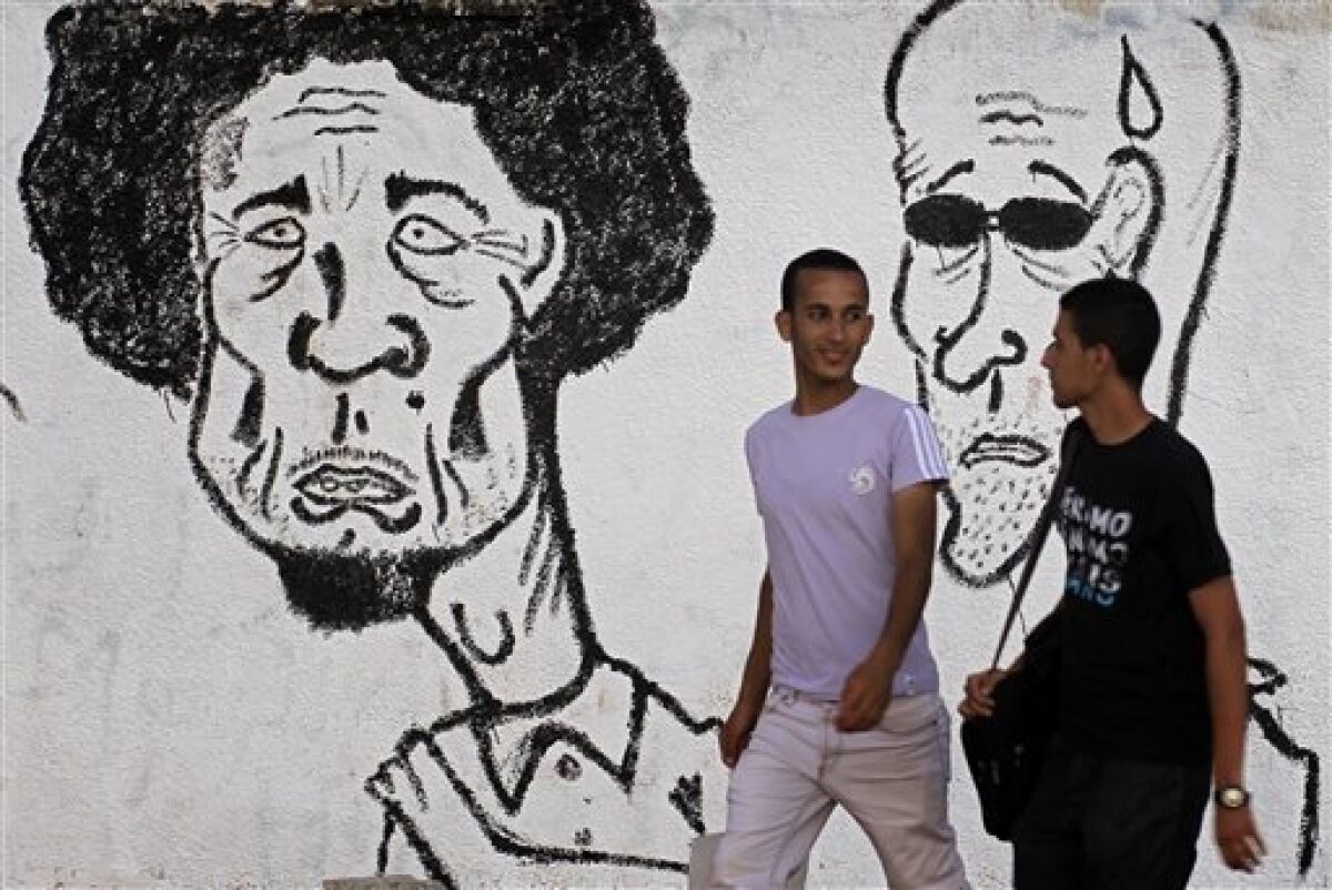 Libyans walk past graffiti depicting Libyan dictator Moammar Gadhafi in the rebel-held Benghazi, Libya, Monday, July 4, 2011. A senior Libyan official said Monday that progress has been made in talks with rebels on ending more than four months of fighting, but a top rebel leader denied that any negotiations are taking place. (AP Photo/Sergey Ponomarev)