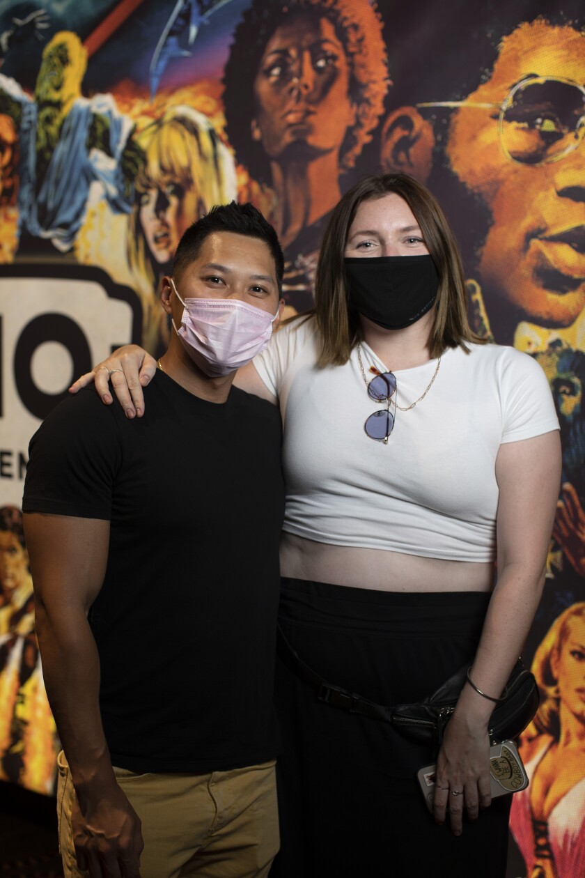 Two people pose in front of a mural