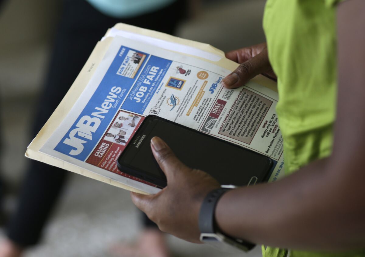 A person holds a job fair flier and phone in their hands.