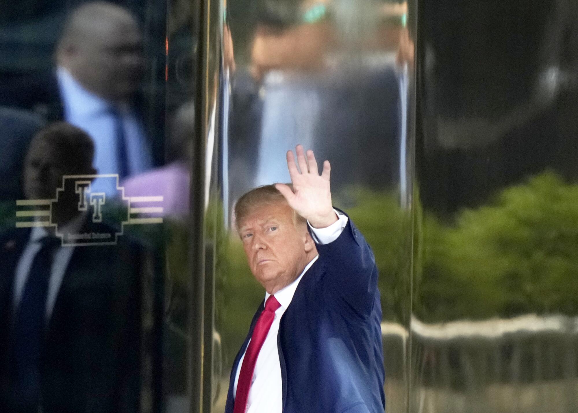 Donald Trump arrives at Trump Tower waving with his left arm while looking at the camera.
