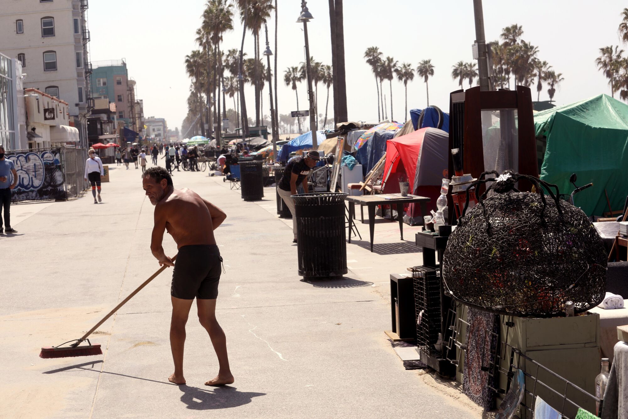 An unhoused man sweeps Ocean Front Walk next to an encampment