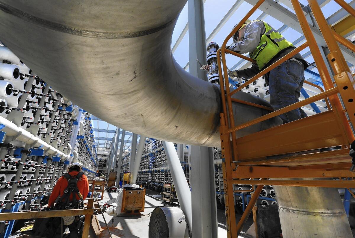 Steven Montes, right, installs a pressure relief valve on a 24-inch stainless steel pipe that will carry desalinated water from the thousands of reverse osmosis filters at the soon-to-be-opened desalination plant in Carlsbad, Calif.