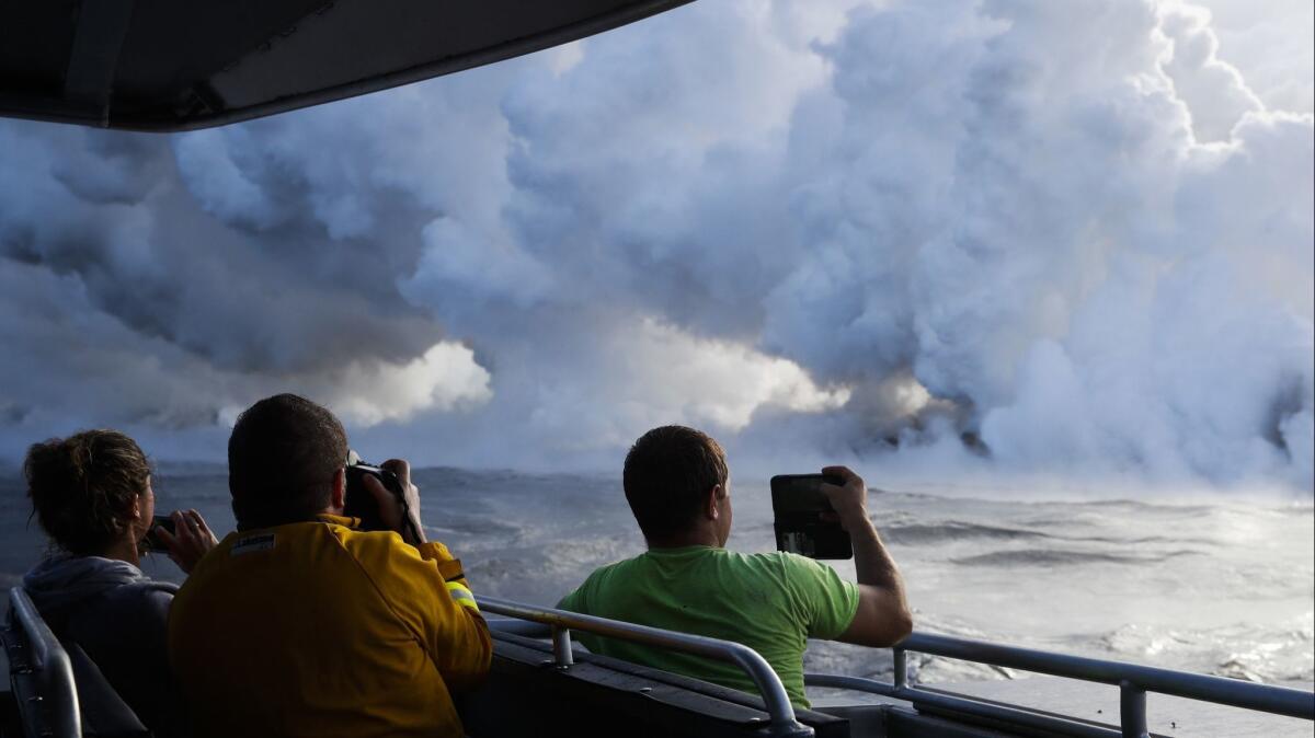 People take pictures as lava pours into the ocean, generating plumes of steam near Pahoa, Hawaii.