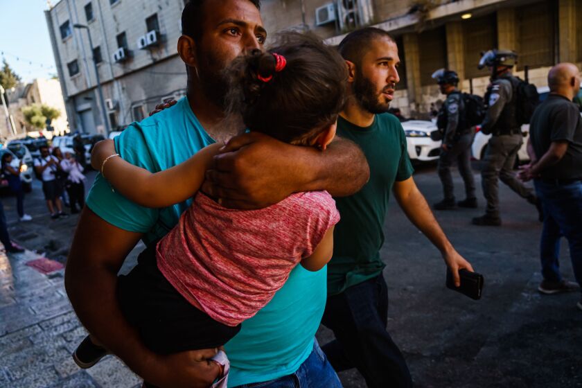 JERUSALEM, ISRAEL -- JUNE 6, 2021: A man carries a child away from the chaos of a panicked crowd as Israeli security forces throw stun grenades to disperse a growing crowd at a news conference calling for the release of Muna al-Kurd and Mohammed al-Kurd, two prominent activists who are residents of the Sheikh Jarrah neighborhood, at a local police station near the Damascus Gate at Old City, in East Jerusalem, Israel, Sunday, June 6, 2021. (MARCUS YAM / LOS ANGELES TIMES)