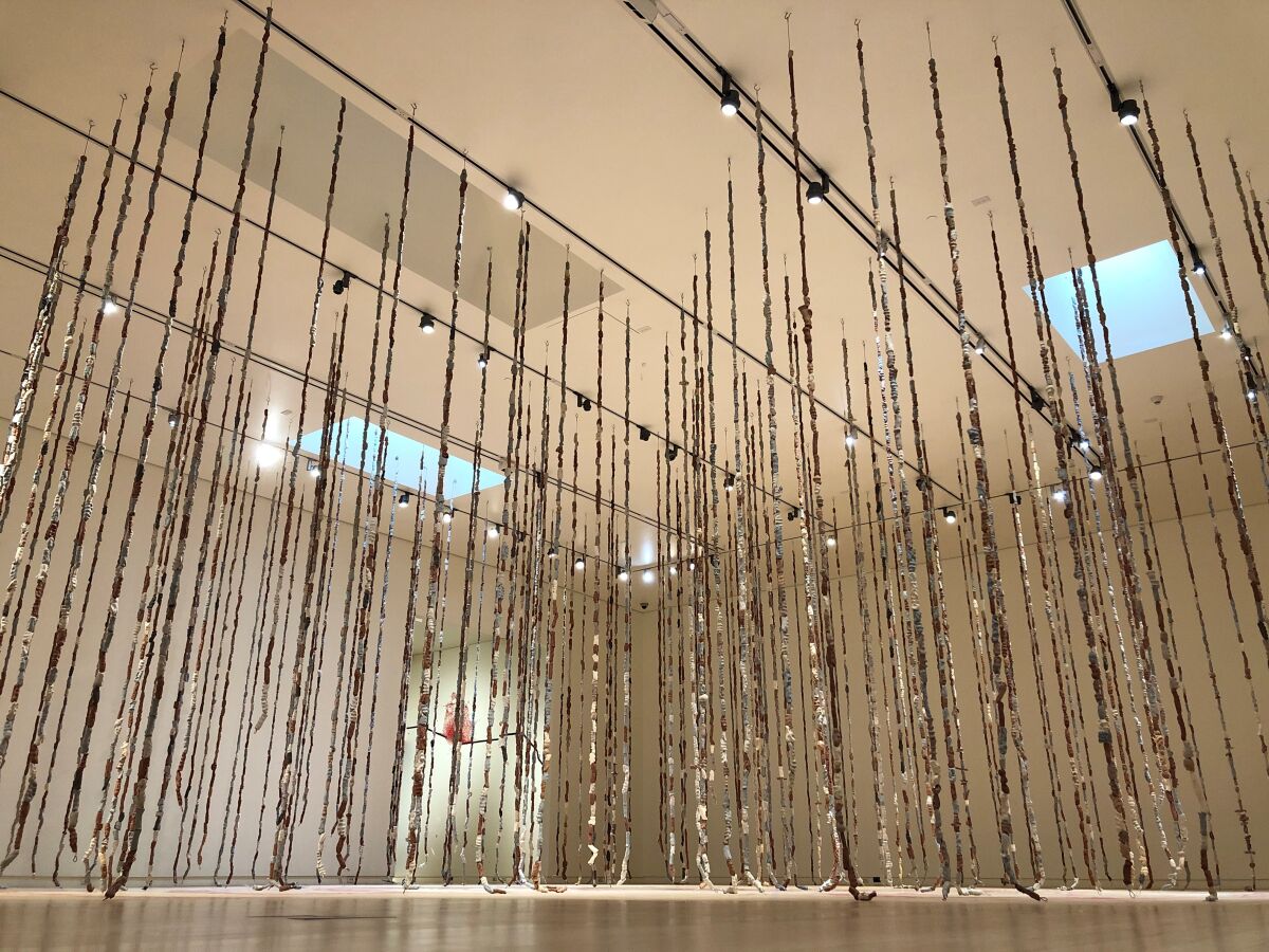 A gallery is filled with long strings of large clay beads hanging from the ceiling in the form of a circular labyrinth.