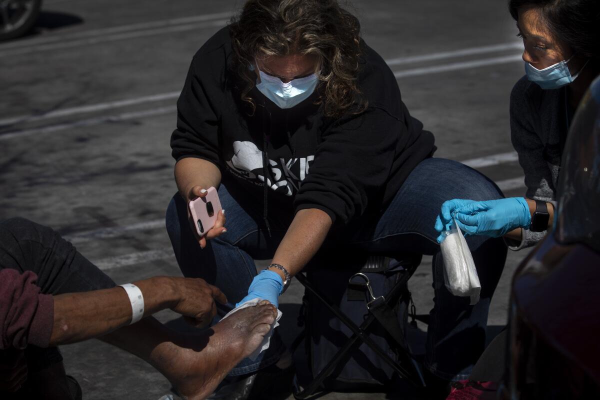 Amid the coronavirus pandemic, Dr. Susan Partovi, middle, and nurse practitioner Jen King, right, administer aid to a man in a Home Depot parking lot in Los Angeles on March 26, 2020.
