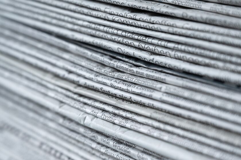 A stack of various daily newspapers on a table.