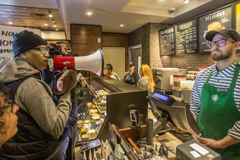Local Black Lives Matter activist Asa Khalif, left, stands inside a Starbucks, Sunday April 15, 2018, demanding the firing of the manager who called police resulting the arrest of two black men on Thursday. The arrests were captured on video that quickly gained traction on social media. (Mark Bryant/The Philadelphia Inquirer via AP)