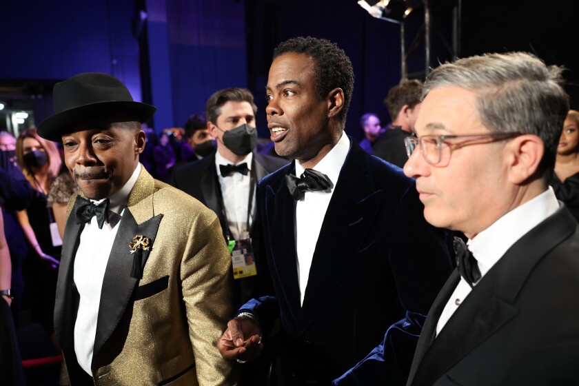 Three men in suits standing in a crowded room.