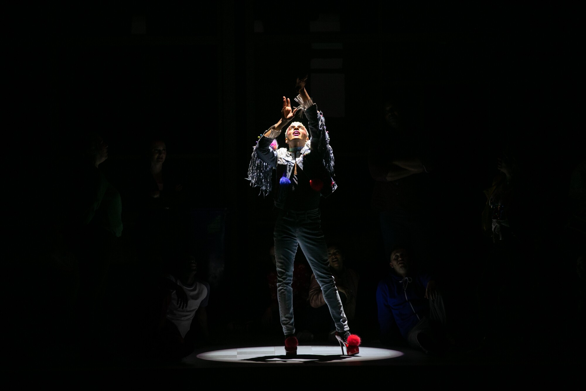 A man stands under a spotlight with his hands raised.