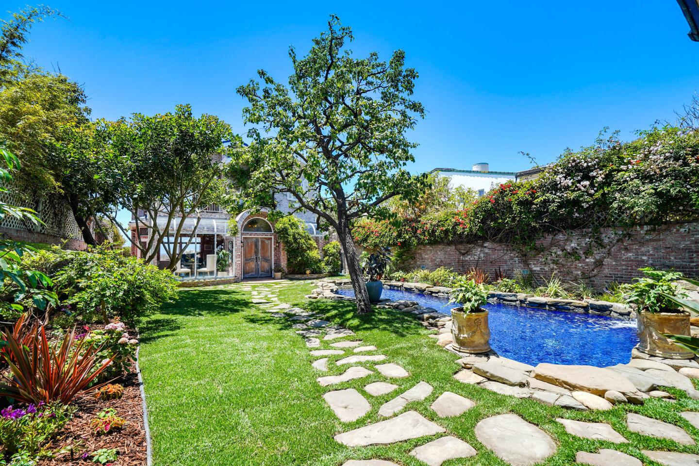 The front yard has grass, trees and a pool.