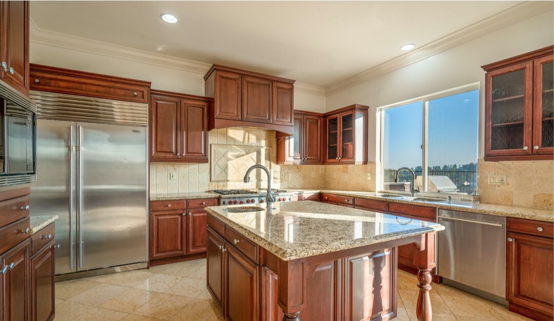 A large center island dominates a kitchen with stainless steel refrigerator and stained-wood cabinetry.